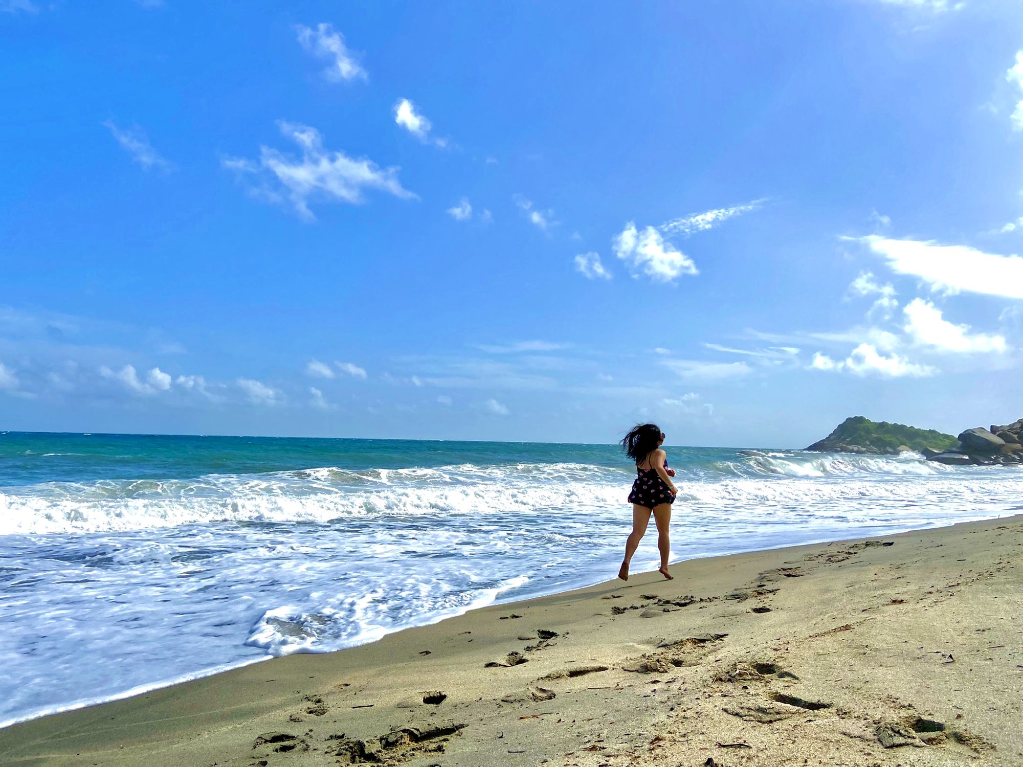 Paulina corriendo descalza por la orilla de una playa, con el mar y un cielo azul de fondo